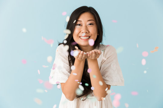 Asian young emotional woman isolated over blue background over confetti.