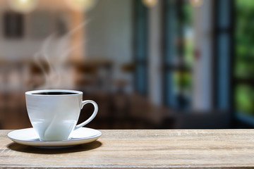 Hot cup of coffee on wooden desk on blurred coffee shop background