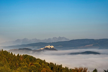Obraz premium Scenic view of Spis Castle in front of majestic High Tatras mountain range surrounded with morning fog/mist in autumn time.