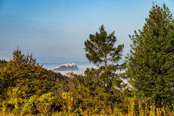 Obraz premium Scenic view of Spis Castle in front of majestic High Tatras mountain range surrounded with morning fog/mist in autumn time.