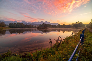 Obraz premium Early morning shot of peaceful scene of beautiful autumn mountain landscape with lake, colorful trees and high peaks and red sky in High Tatras, Slovakia.