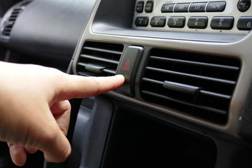 A young Asian woman finger is pushing the emergency sign button at a car console to request a help.