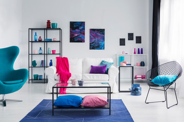 Colorful living room with white sofa, blue armchair and cosmos graphics on the wall, real photo