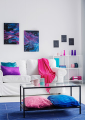 Vertical view of stylish living room with comfortable white couch with pink blanket and blue and purple pillows, cosmos graphics on the wall, real photo
