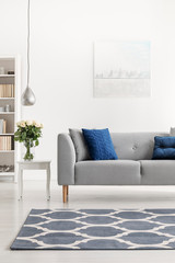 Patterned carpet in front of grey couch with blue pillows in white loft interior with flowers. Real photo