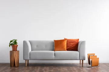 Foto op Plexiglas Comfortable couch with orange and red pillow in spacious living room interior, real photo with copy space on the empty white wall © Photographee.eu
