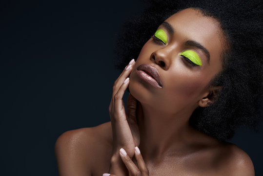 portrait of beautiful african american model with bright neon makeup and bare shoulders isolated on black