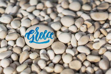 Greece word calligraphy on white pebble with copy space on the right.