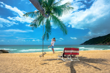 view of sweet lover enjoy together happy on the sea beach in romantic honeymoon, with deck chair and swing underr shadow of plam coconut tree