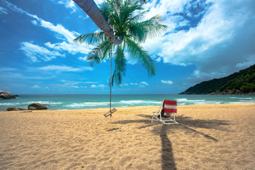 day view of sun sand sea beach with single wood swing and deck chair beach under shadow of coconut tree, relax, comfort and feel free traveling in holidays and vacation