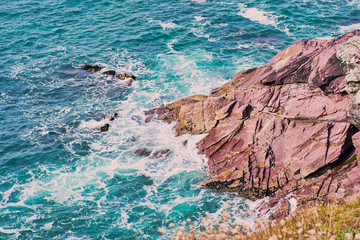 turquoise water around typical slate red rocks on the coast of Cornwall near Polzeath