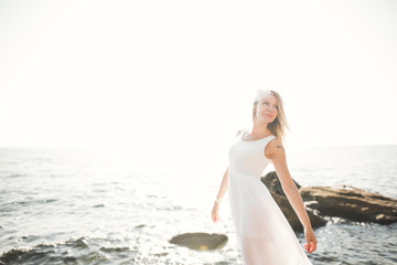 Romantic beautiful bride in white dress posing on the sea stones