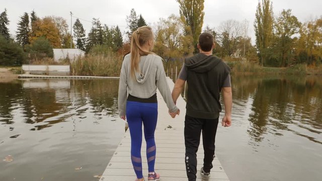Young people sports couple walking holding hands near lake waterline in the morning