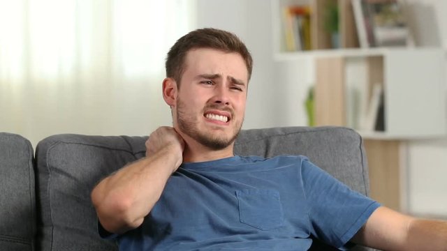 Man suffering neck ache sitting on a couch at home