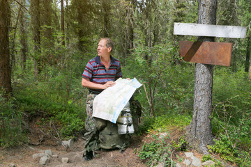 Tourist with a map near the pointers, a place for text. A man searches the road in the forest holds a map near the pointers on the tree.
