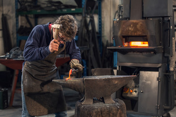 Young blacksmith working with red hot metal