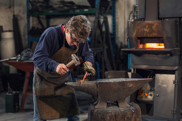 Young blacksmith working with red hot metal