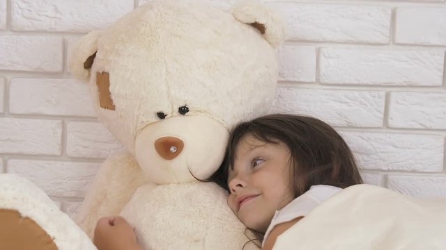 Happy child with a teddy bear. The little girl is sleeping with a big bear.