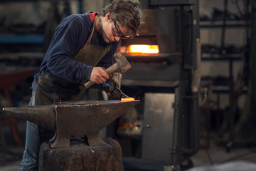 Young blacksmith working with red hot metal