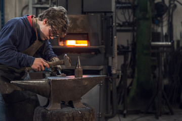 Young blacksmith working with red hot metal