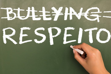 Fototapeta premium Female hand writing with chalk on green chalkboard Bullying and Respect (in portuguese).