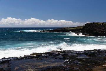 Fototapeta na wymiar Shoreline on Big Island of Hawaii near South Point. Deep blue Pacific ocean, waves breaking on the black lava rock of the coastline. Small tidepool in the foreground.