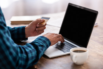 cropped shot of man holding credit card and using laptop with blank screen