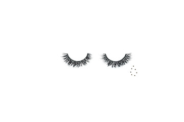 Dramatic black long false eyelashes placed in the shape of a human eye decorated with a teardrop of golden glitter isolated on white background shot with studio light