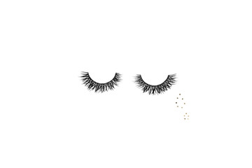 Dramatic black long false eyelashes placed in the shape of a human eye decorated with two teardrops of golden glitter isolated on white background shot with studio light