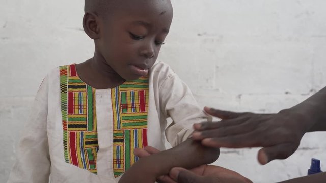Spraying a malaria prevention liquid on a African black child's hands. 4K RAW clip, please modify and edit (color grade, stabilize, etc.) in postproduction.