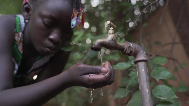 Young beautiful African teenage girl getting her water from a tap in her village. 4K RAW clip, please modify and edit (color grade, stabilize, etc.) in postproduction.