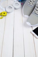 Sport sneakers , smartphone, earphones and yellow measure tape on white wooden background