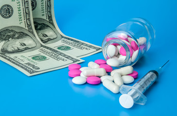 Syringe, dollars and pink and white pills on a bright blue background.