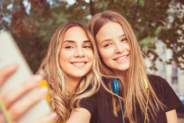 two friends girls with smartphone beautiful close up outdoor making selfie, teen trendy hairstyle and make up autumn colors sunshine day 