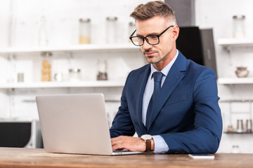 Fototapeta na wymiar handsome businessman in eyeglasses using laptop at home