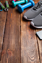 Smartphone, sport shoes and dumbbells on wooden background