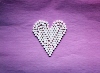 white pills laid out in the shape of a heart on a pink background. concept - heart disease, heart disorders and drugs, cardiology.