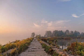 Mglisty wschód słońca nad rzeką z drogą na pierwszym planie i zagrodą dla zwierząt z tyłu.
