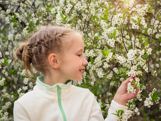 Beautiful girl in sportswear admires the beauty of cherry blossoms in the spring garden.