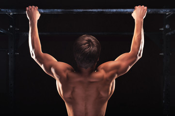 Fototapeta na wymiar Rear view of muscular man doing pull up exercise on horizontal bar. Male athlete working out in the gym