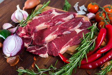 Fresh slices of beef with rosemary and vegetables assortment on wooden desk