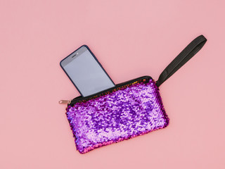 Phone and shiny purple women's handbag on pink background. Flat lay.