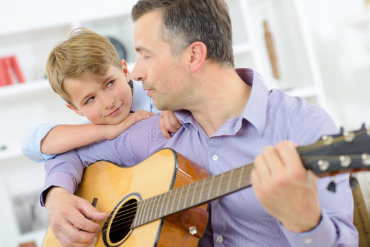 Man playing guitar, child leaning on his shoulder