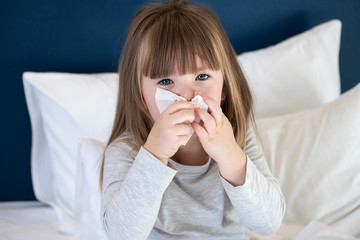 cold sick child laying on bed and blowing her nose in tissue