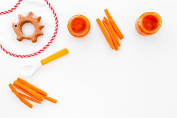 Healthy food for small babies. Carrot puree in bowl near bib, carrot slices, spoon on white background top view copy space