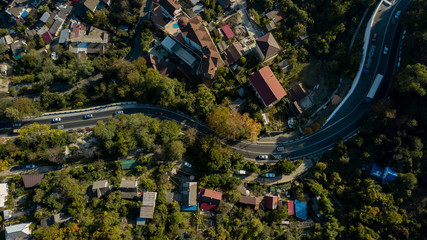 Aerial view of curvy rural road in mountains in autumn season. Cars driving below on the road.