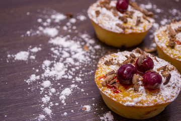 Cupcakes with cherries and powdered sugar and chocolate chips on a dark wooden table.