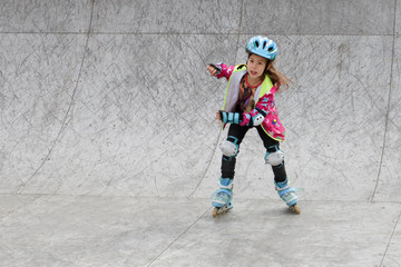 Little girl riding on roller skates in a helmet and knee pads