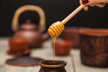 Tea ceremony, tea party. Clay dishes. Honey flows from a wooden spoon into a pot