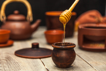 Tea ceremony, tea party. Clay dishes. Honey flows from a wooden spoon into a pot